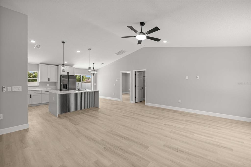 An open-concept kitchen and living area features light wood flooring, white cabinetry, and a kitchen island — 85 JUNIPER LOOP CIRCLE, OCALA, FL