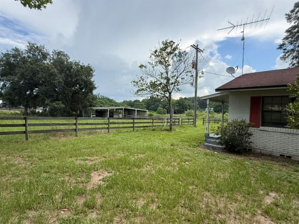 A view of a grassy yard with a wooden fence, a shed, and a house — 5890 SE 145TH STREET, SUMMERFIELD, FL