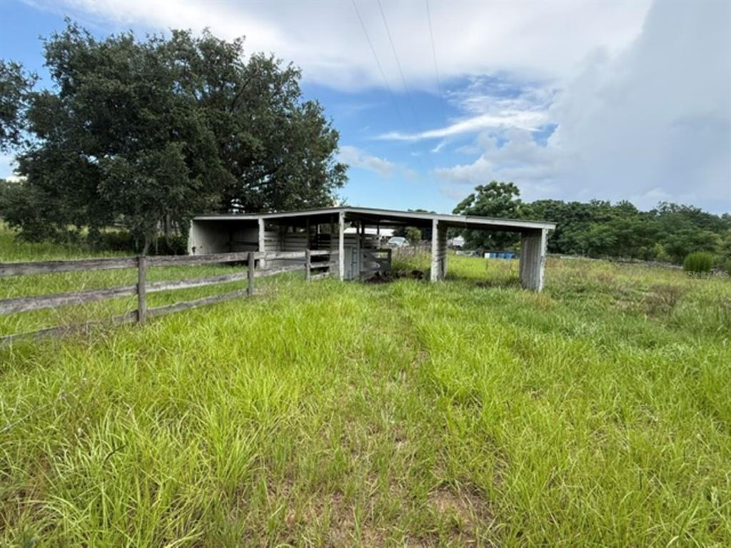 A wooden fence surrounds a grassy field with an open-sided metal shed and trees — 5890 SE 145TH STREET, SUMMERFIELD, FL