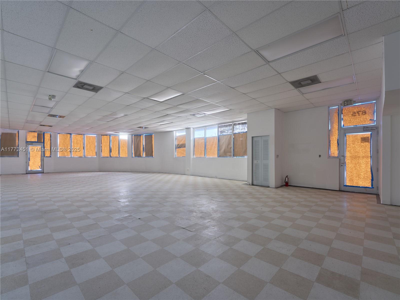 An empty commercial space features a drop ceiling, checkered tile flooring, and windows covered with paper — 6211 NW 7th Ave # 75, Miami FL 33150, MIAMI, FL