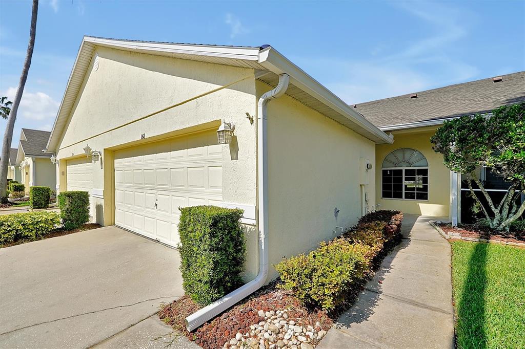 A light yellow house exterior features a two-car garage, a concrete walkway, and manicured landscaping — 168 CLUB VILLAS LANE, KISSIMMEE, FL