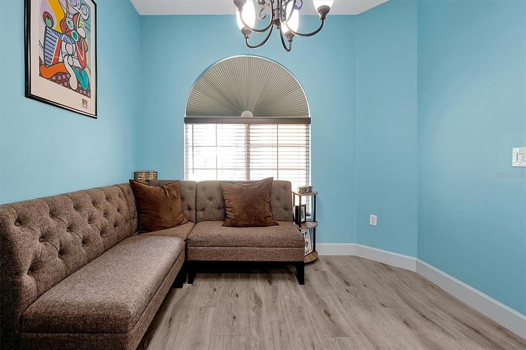 A room with light blue walls, wood-look flooring, an arched window, and a brown sectional sofa — 168 CLUB VILLAS LANE, KISSIMMEE, FL