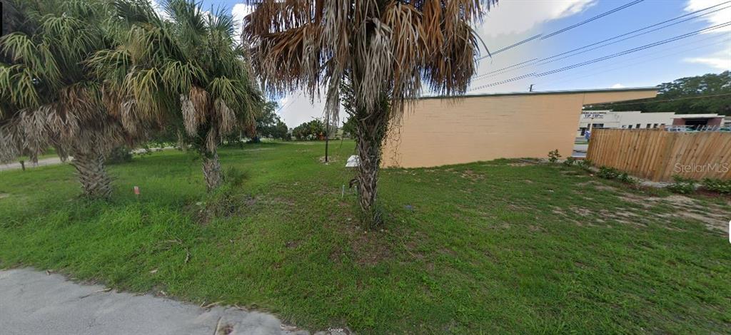 A grassy vacant lot features several palm trees next to a low, peach-colored masonry building — 60 E STREET, LAKE WALES, FL