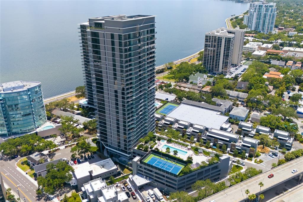 An aerial view shows a tall glass residential tower with a rooftop tennis court — 3015 S YSABELLA AVENUE UNIT 2102, TAMPA, FL