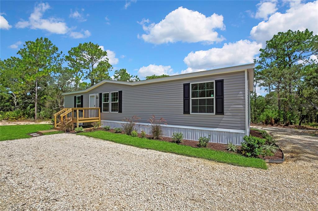 A single-story manufactured home with grey siding and a wooden deck sits on gravel — 5611 W ROCHELLE STREET, HOMOSASSA, FL