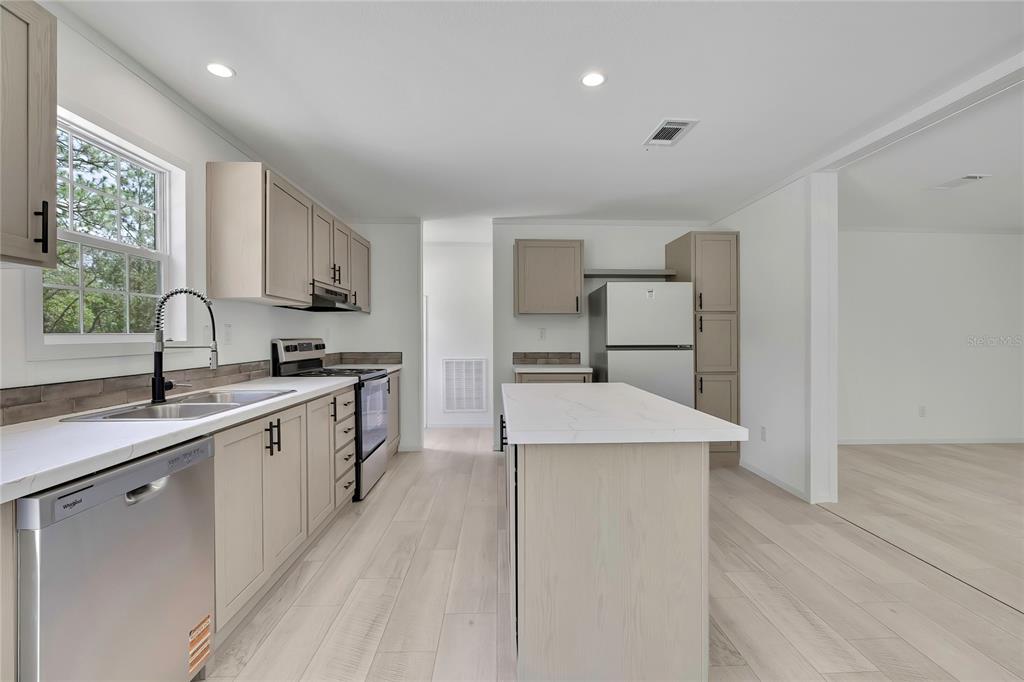 A kitchen features light wood cabinets, white countertops, stainless steel appliances, and light wood flooring — 5611 W ROCHELLE STREET, HOMOSASSA, FL