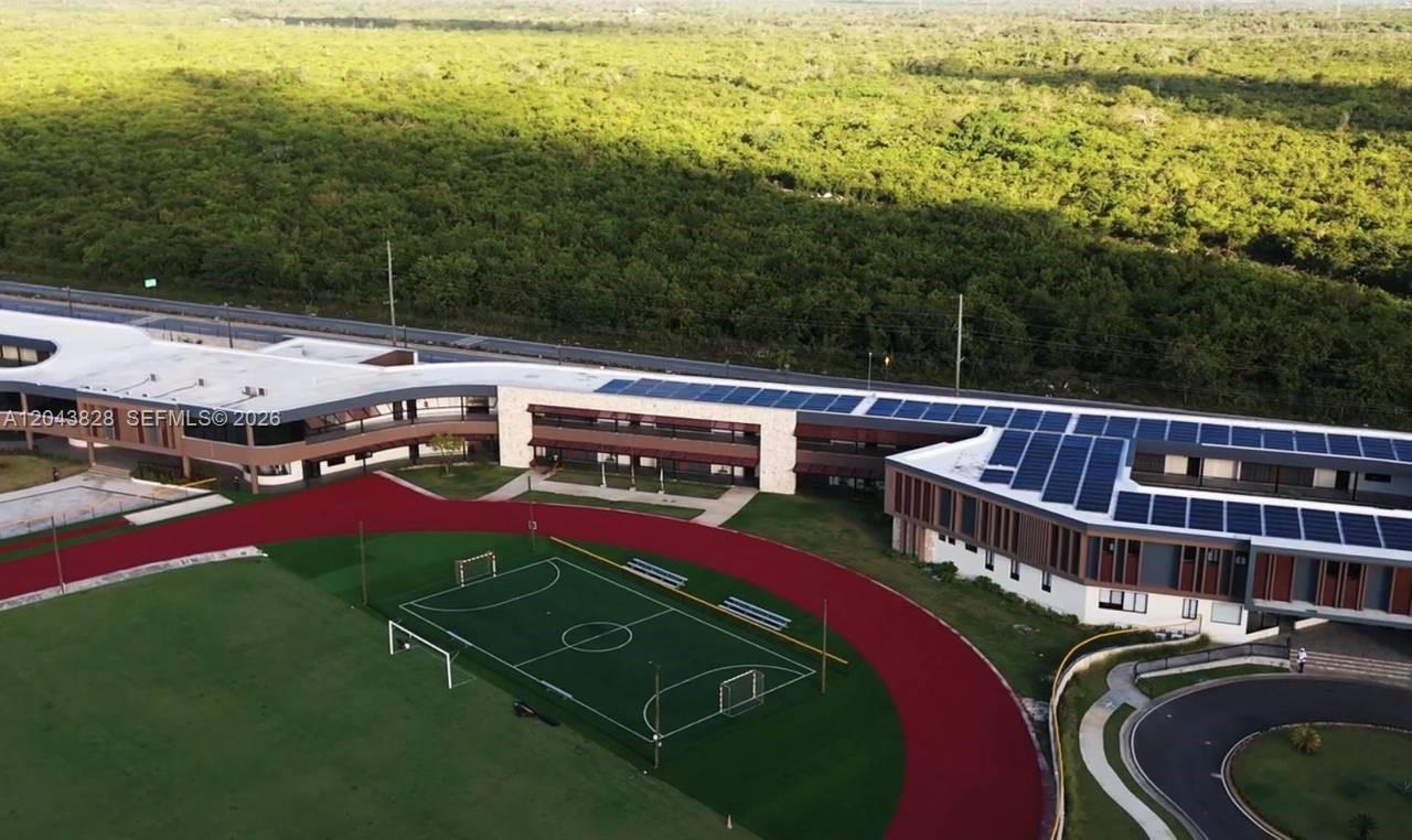 An aerial view of a modern school building with solar panels and an adjacent sports field — vistta cana, FL