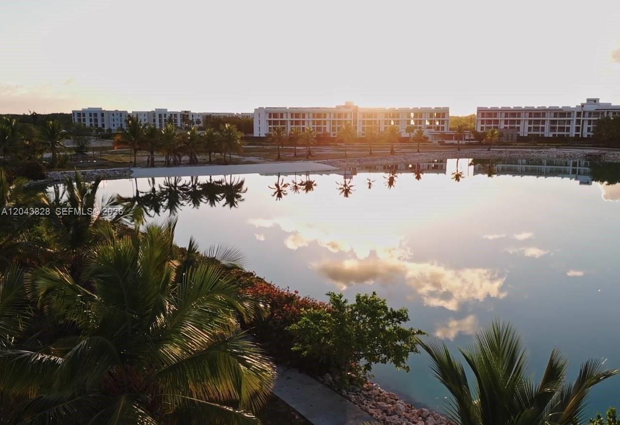 A calm lake reflects palm trees and a large apartment complex at sunset — vistta cana, FL