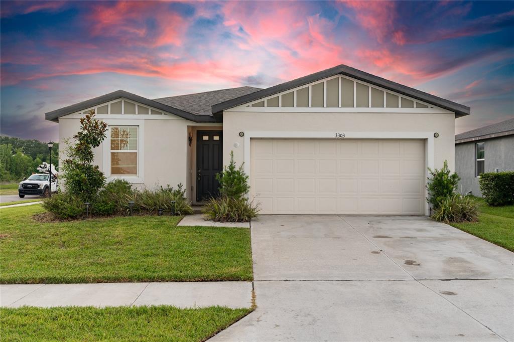 An aerial view shows a suburban house with a pond in the background at sunset — 3303 ASHER MOON LANE, ZEPHYRHILLS, FL