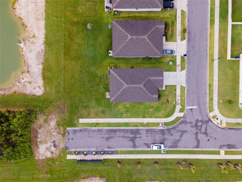 An aerial view shows two suburban houses with driveways situated near a pond and road — 3303 ASHER MOON LANE, ZEPHYRHILLS, FL