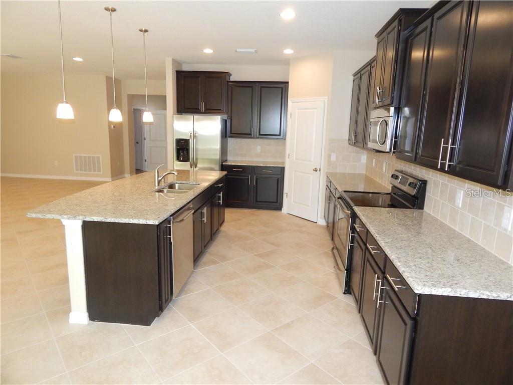 A kitchen features dark wood cabinets, granite countertops, a large island, and stainless steel appliances — 15302 LAS OLAS PLACE, BRADENTON, FL