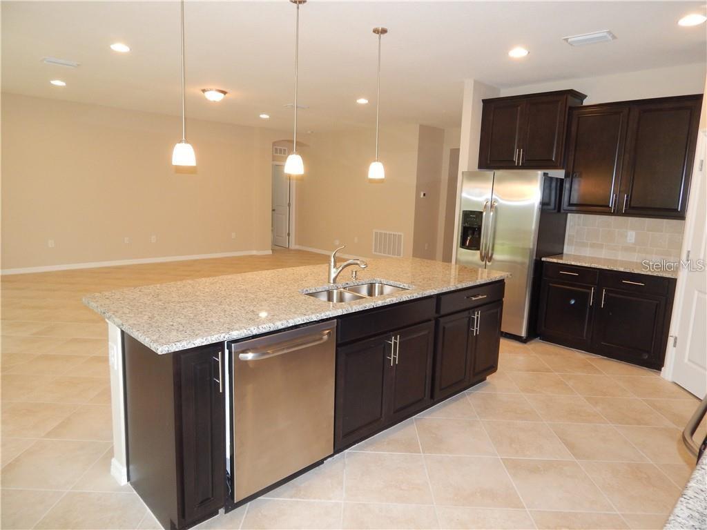 A kitchen features a granite-topped island, stainless steel appliances, and dark wood cabinetry — 15302 LAS OLAS PLACE, BRADENTON, FL