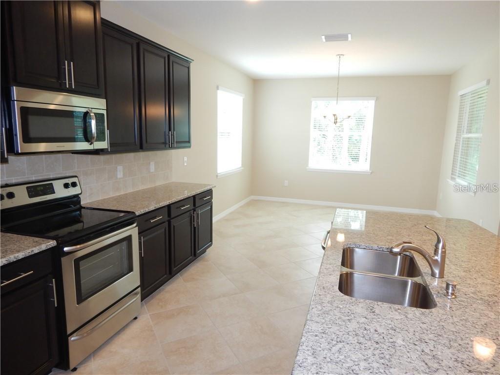 A kitchen features dark wood cabinets, granite countertops, stainless steel appliances, and tile flooring — 15302 LAS OLAS PLACE, BRADENTON, FL