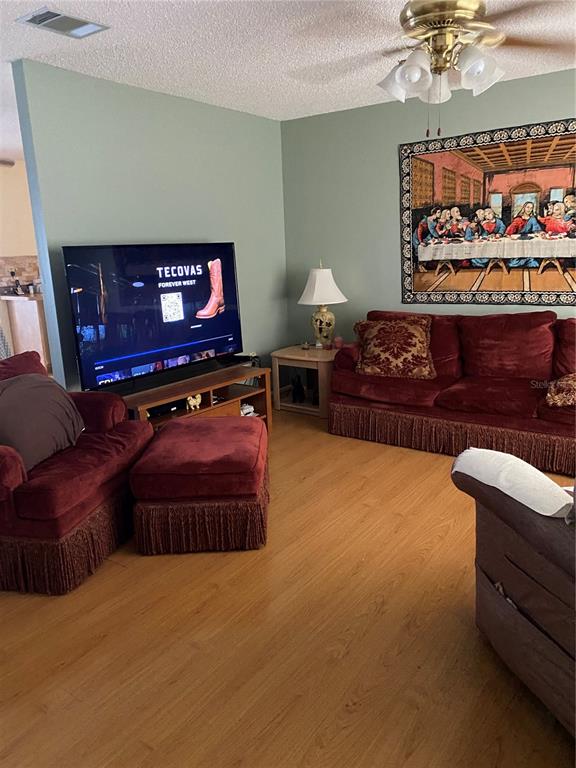 A living room features light green walls, wood flooring, a red sofa, and a television — 8503 GAILLARD AVENUE, NORTH PORT, FL