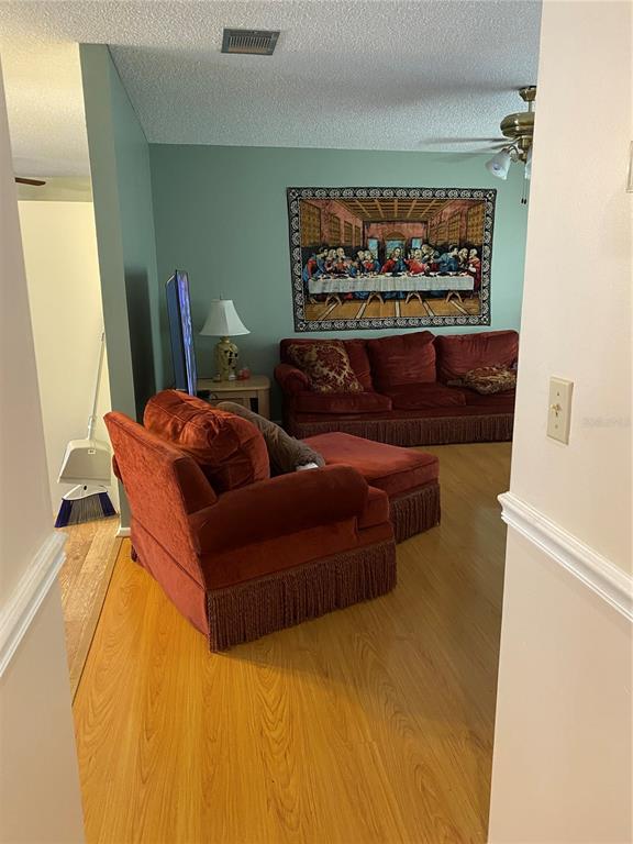 A living room features wood-look flooring, a red velvet sofa and chair, and a wall tapestry — 8503 GAILLARD AVENUE, NORTH PORT, FL