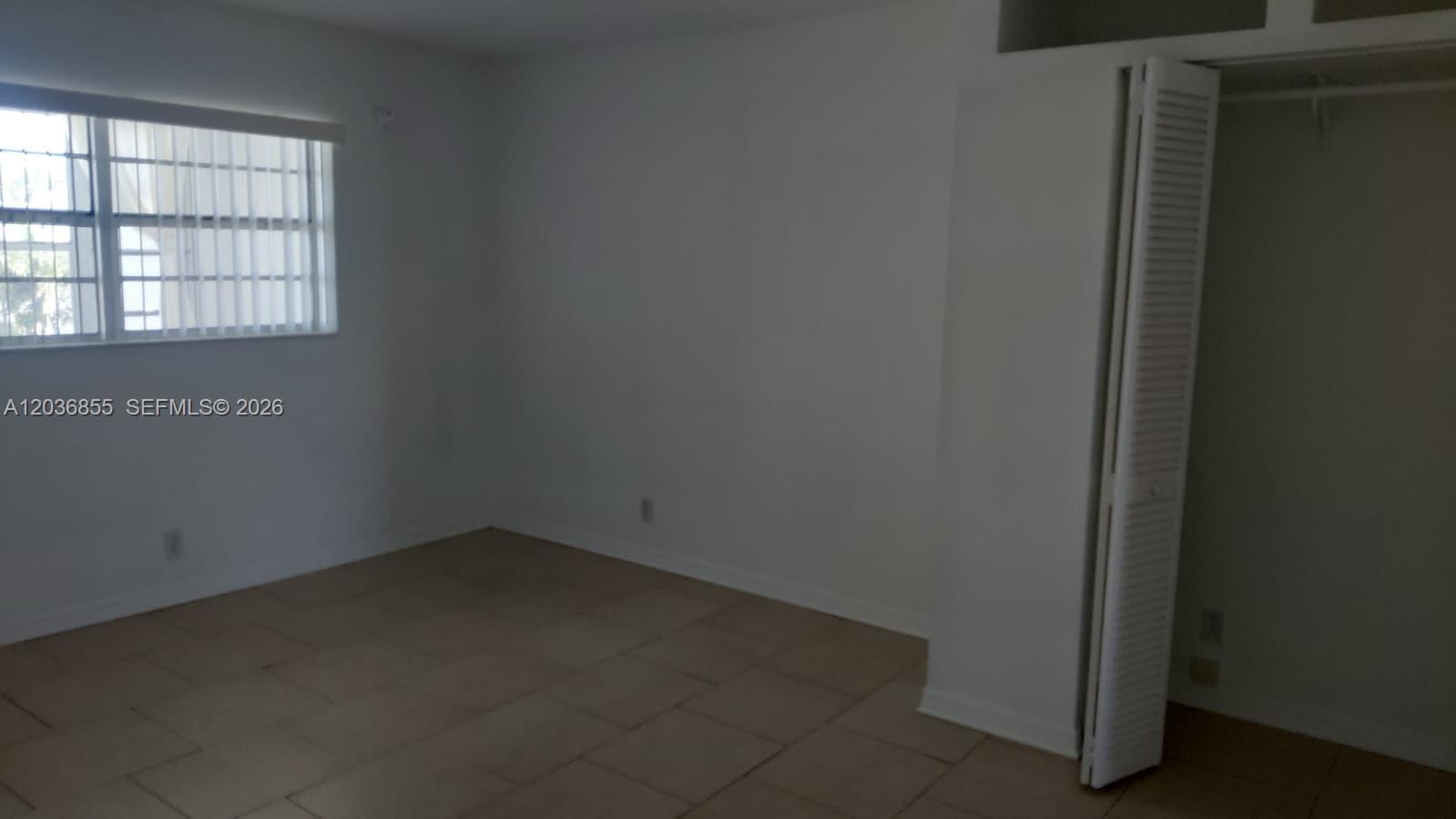 An empty bedroom features white walls, tile flooring, a window with blinds, and a closet — 7897 Golf Cir Dr # 306, Margate FL 33063, MARGATE, FL