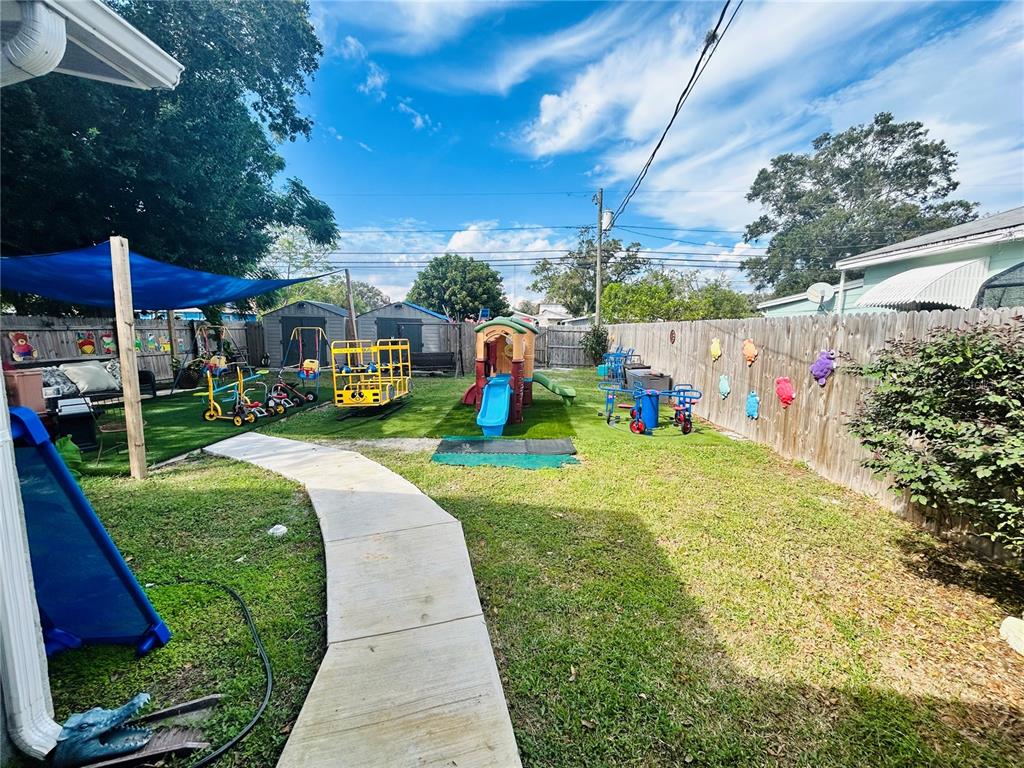 A backyard play area features artificial turf, a plastic slide, and various children's riding toys — 4611 14TH AVENUE S, ST PETERSBURG, FL