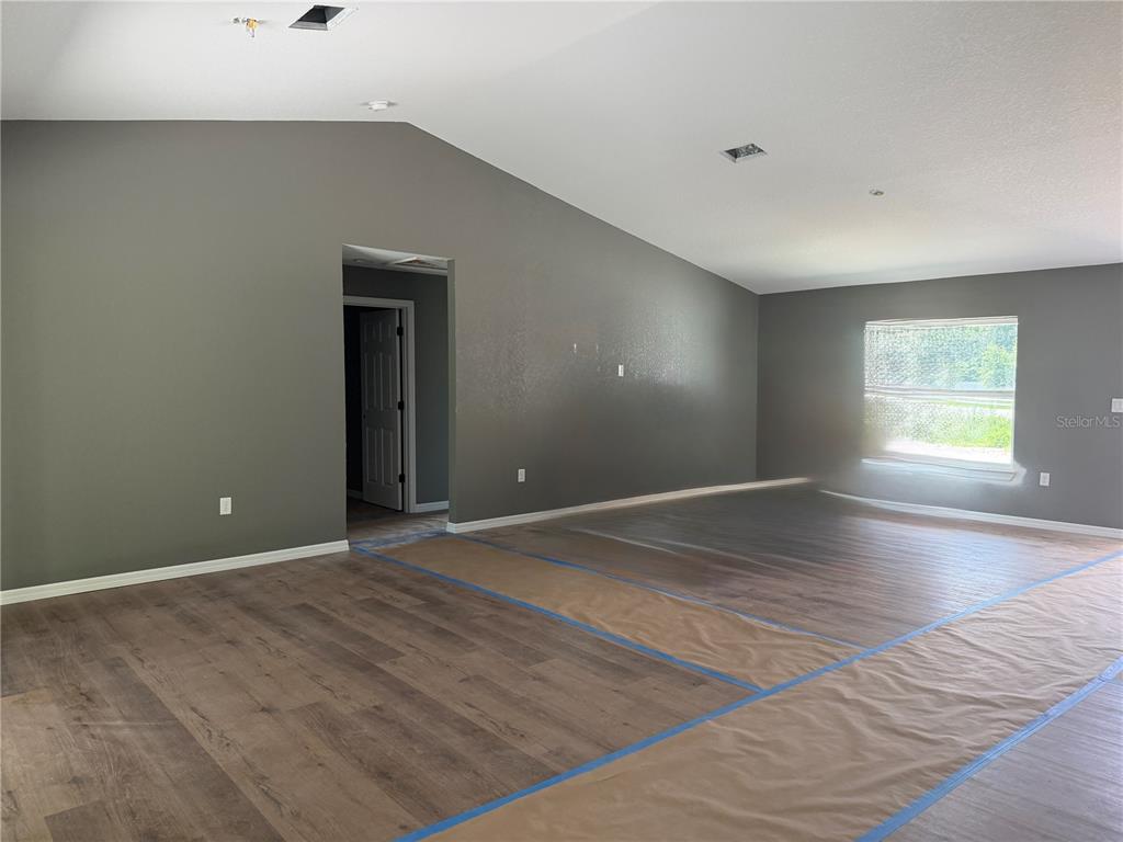 A spacious room with vaulted ceilings, gray walls, and wood-look flooring under construction — 4869 SE 24TH STREET, OCALA, FL