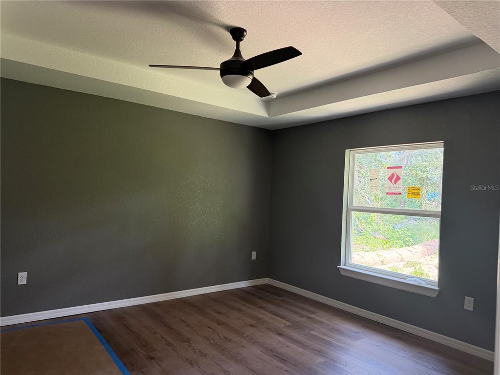 A bedroom with gray walls, wood-look flooring, a tray ceiling, and a ceiling fan — 4869 SE 24TH STREET, OCALA, FL