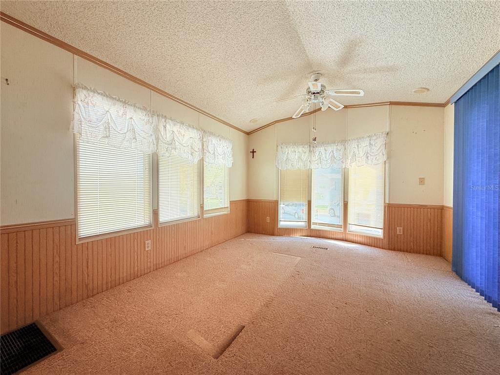 An empty room with beige carpet, wood-paneled wainscoting, and multiple windows with white valances — 2215 73RD STREET E UNIT 275, PALMETTO, FL