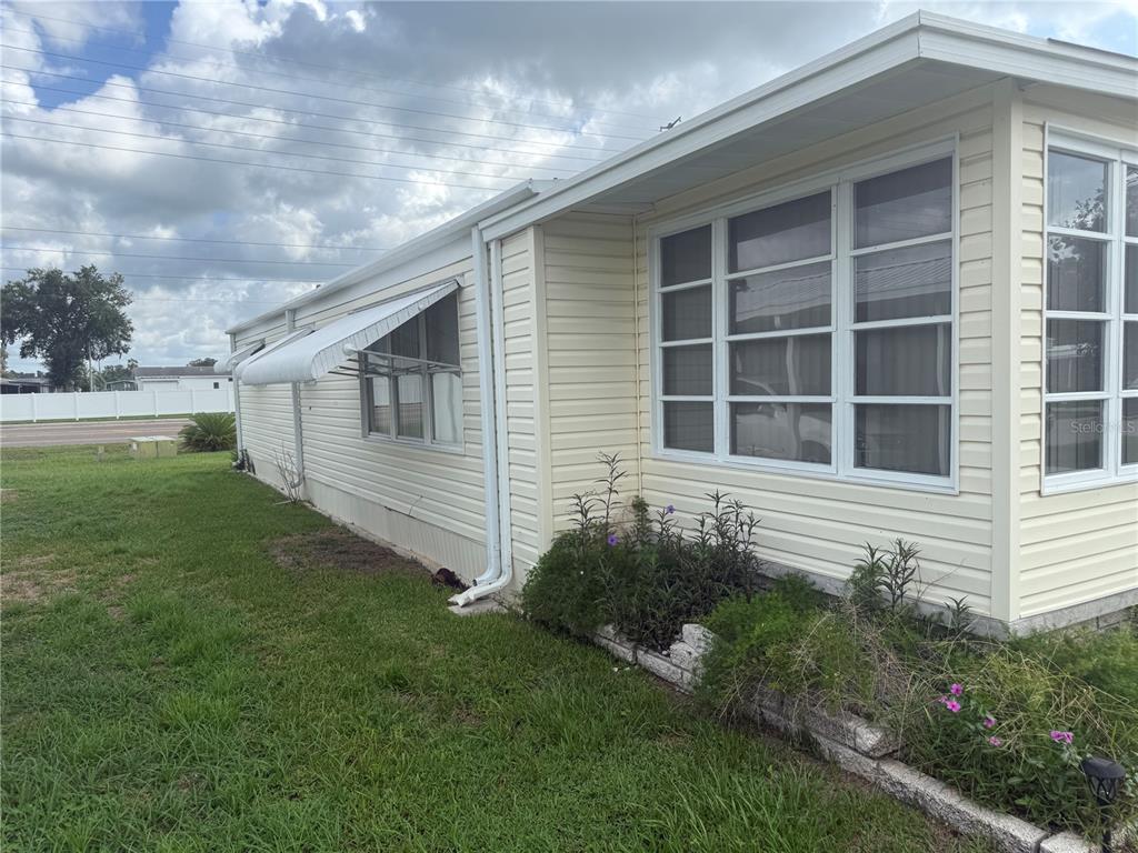The exterior side of a light-colored mobile home features vinyl siding, windows, and landscaping — 37529 ATTICA AVENUE, ZEPHYRHILLS, FL