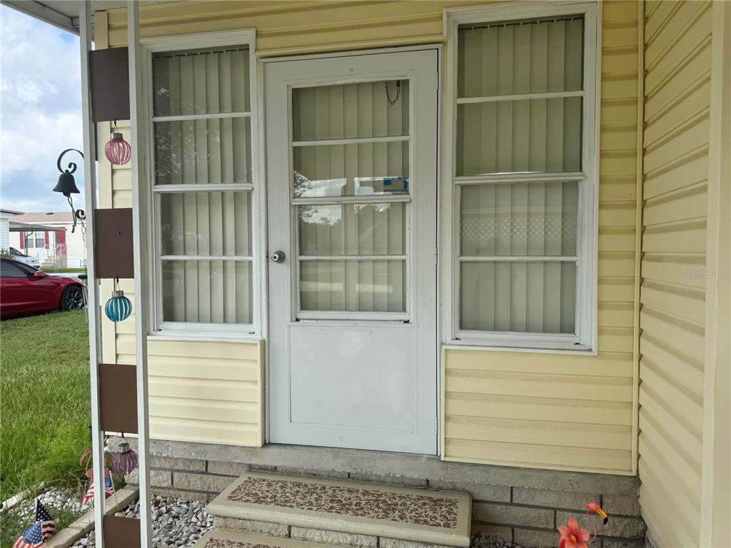 A yellow-sided home exterior features a white storm door flanked by two windows — 37529 ATTICA AVENUE, ZEPHYRHILLS, FL