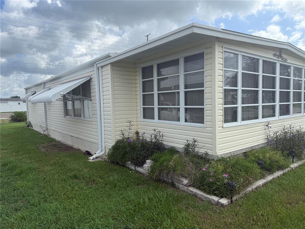 A light-colored mobile home features a large sunroom with many windows and a garden bed — 37529 ATTICA AVENUE, ZEPHYRHILLS, FL
