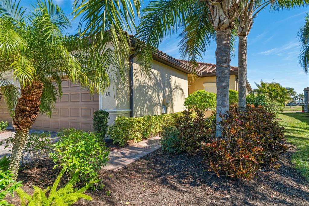 A beige house exterior features a garage, a paved walkway, and several palm trees — 131 BABBLING BROOK RUN, BRADENTON, FL