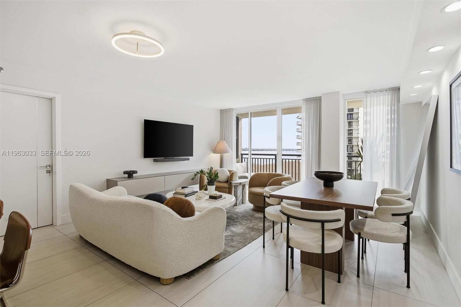 A modern living and dining area features a white sofa, wooden table, and balcony view — 540 Brickell Key Dr # 823, Miami FL 33131, MIAMI, FL