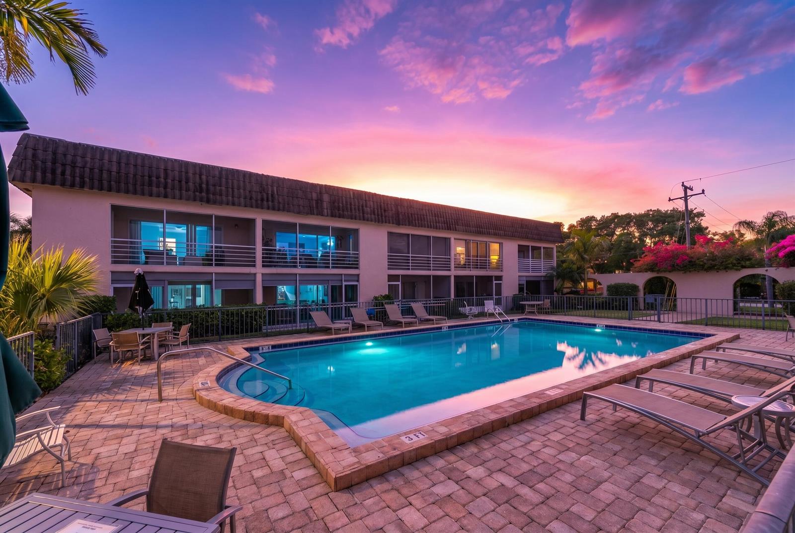 An outdoor swimming pool sits in front of a two-story building at sunset — 342 Southwind Drive # 118, North Palm Beach FL 33408, NORTH PALM BEACH, FL
