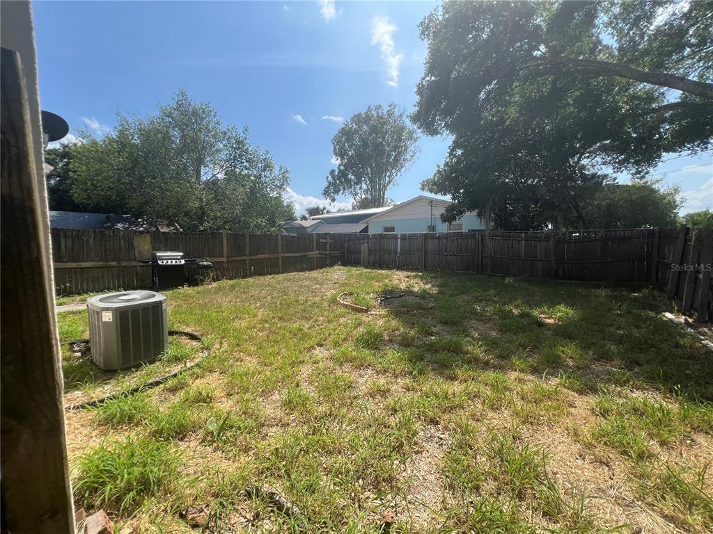 A fenced backyard features a patch of grass, an air conditioning unit, and a grill — 1120 S MARY STREET, EUSTIS, FL