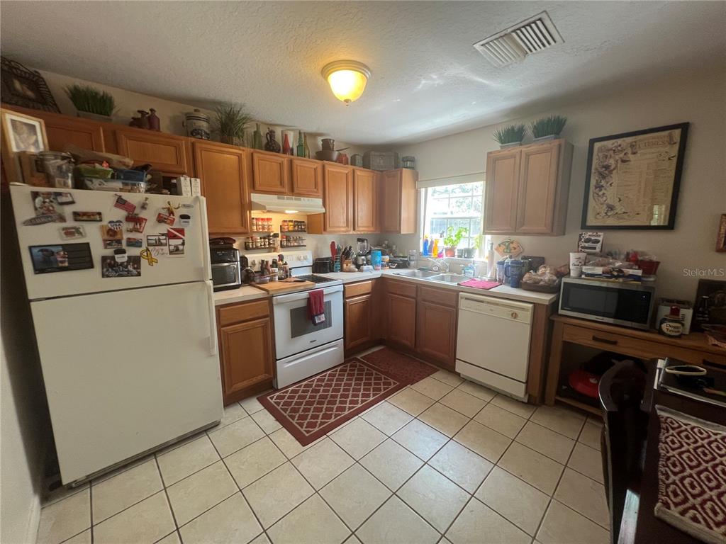 A kitchen with wood cabinets, white appliances, tile flooring, and a window above the sink — 1120 S MARY STREET, EUSTIS, FL