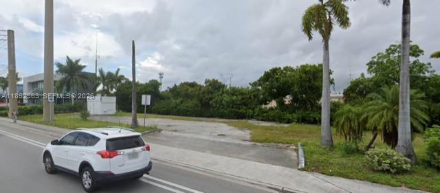 A white SUV drives past a vacant, paved lot with palm trees and dense vegetation — 18560 Biscayne Blvd, Aventura FL 33180, AVENTURA, FL