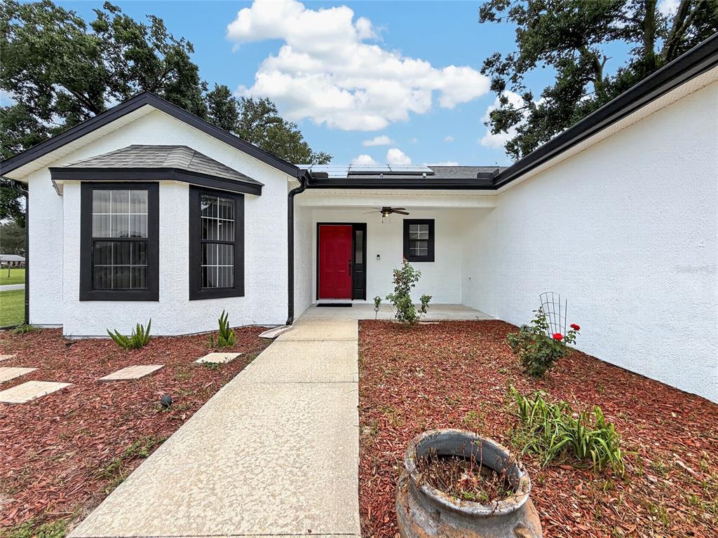 A white house exterior features a red front door, black window frames, and a walkway — 370 CARRIAGE LANE, LADY LAKE, FL