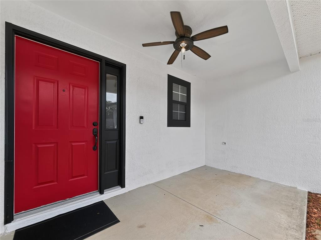 A covered porch features a bright red front door, a ceiling fan, and white walls — 370 CARRIAGE LANE, LADY LAKE, FL