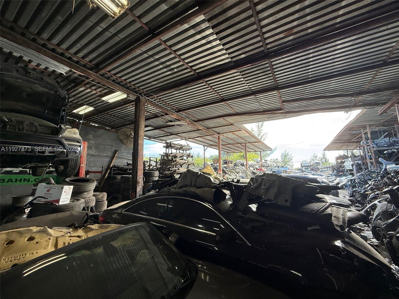 An open-air warehouse contains stacked car parts, tires, and several vehicles in various states — 12755 Cairo Ln, Opa-Locka FL 33054, OPA-LOCKA, FL