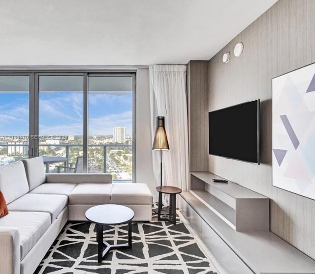 A modern living room features a sectional sofa, a television, and a view of buildings — 4010 S Ocean Dr # R1206, Hollywood FL 33019, HOLLYWOOD, FL