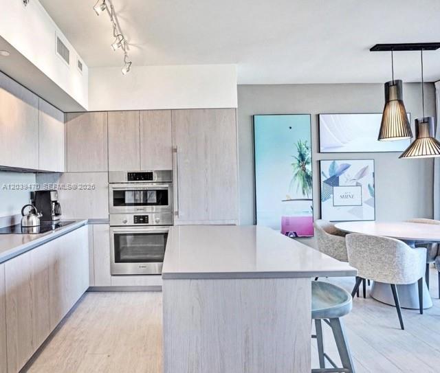 A modern kitchen features light wood cabinets, stainless steel appliances, and a central island — 4010 S Ocean Dr # R1206, Hollywood FL 33019, HOLLYWOOD, FL
