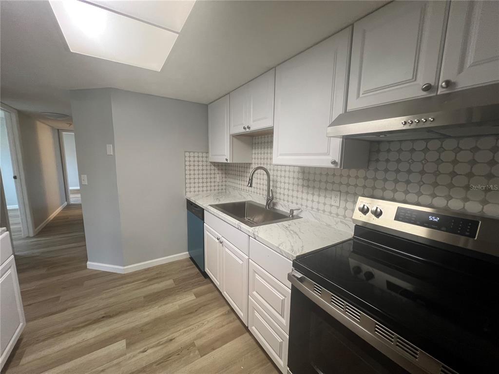 A kitchen features white cabinets, marble-look countertops, a stainless steel stove, and a tile backsplash — 4022 BEAVER LN NE UNIT 800 C, PORT CHARLOTTE, FL