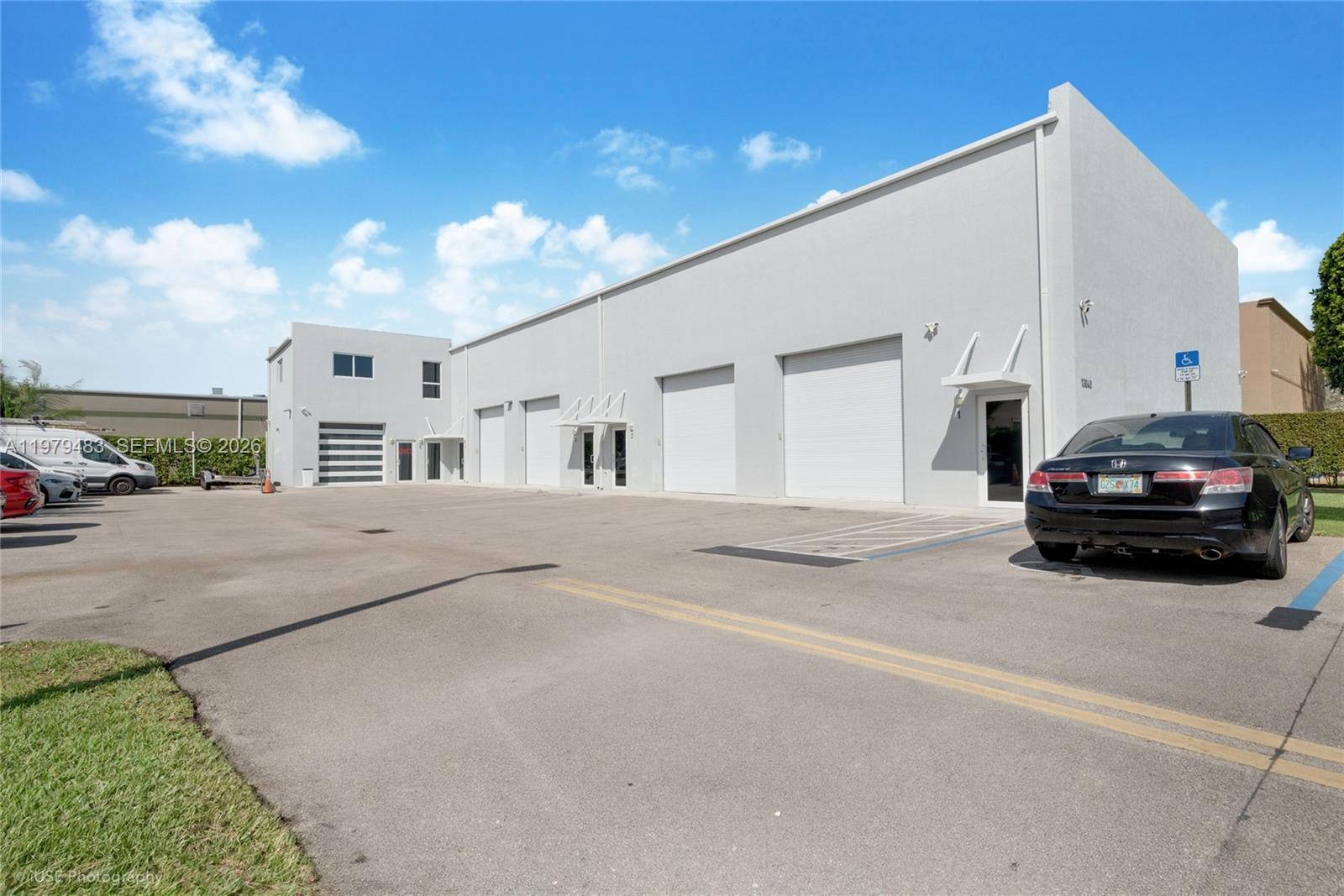 A modern, light-colored industrial warehouse building features multiple roll-up doors and a paved parking lot — 13040 SW 123rd Ave, Miami FL 33186, MIAMI, FL