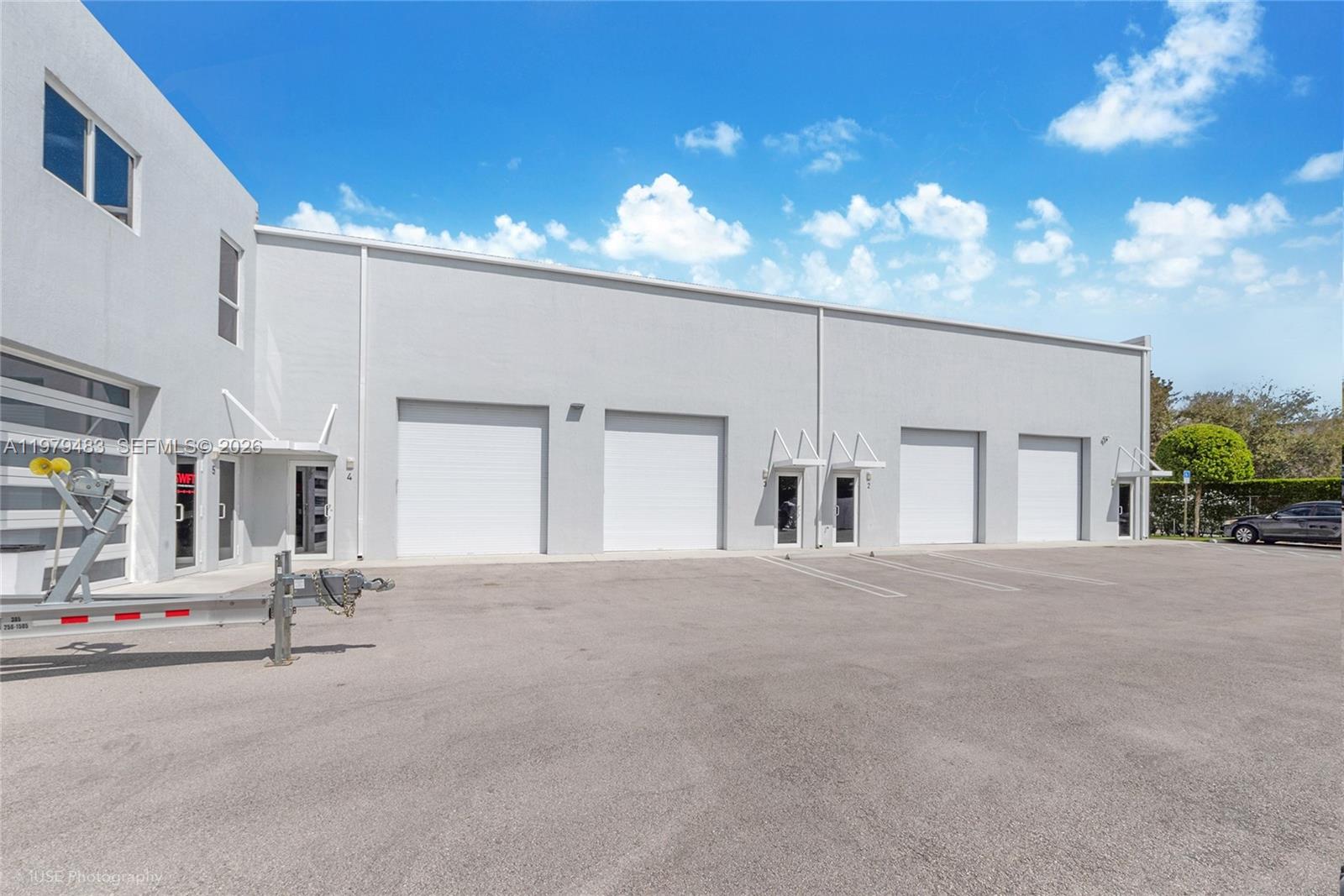 An exterior view of a commercial warehouse building with multiple roll-up doors and glass entryways — 13040 SW 123rd Ave, Miami FL 33186, MIAMI, FL