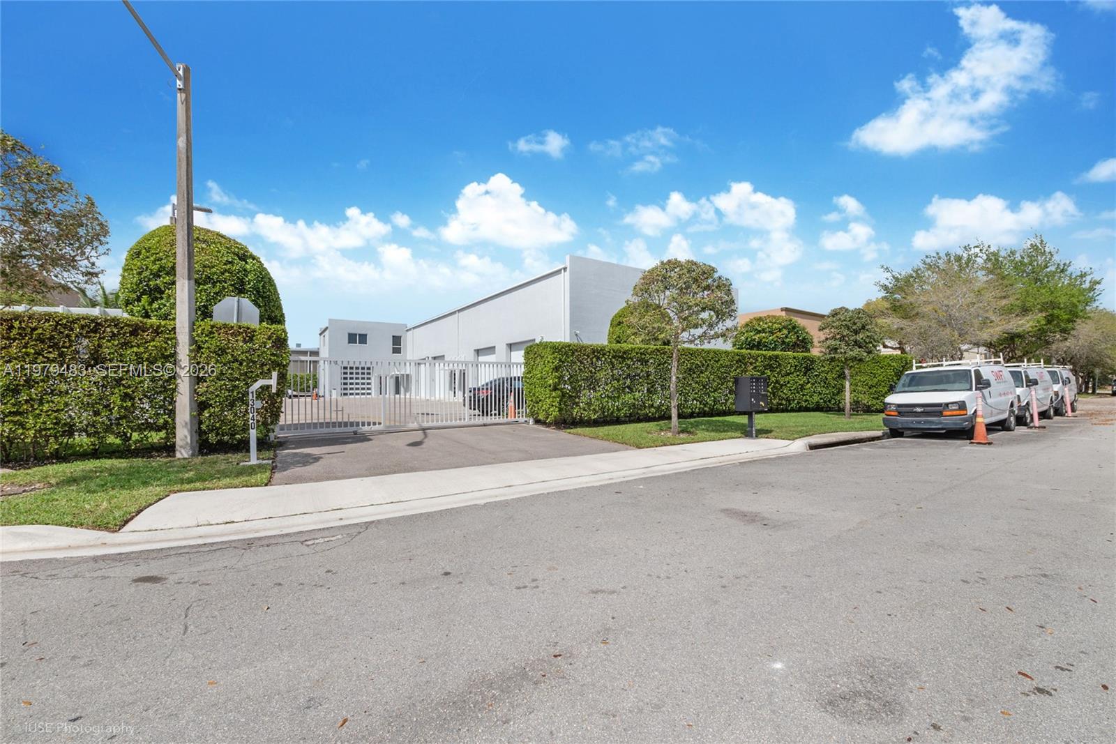 A white industrial building is enclosed by a gated fence and tall green hedges — 13040 SW 123rd Ave, Miami FL 33186, MIAMI, FL