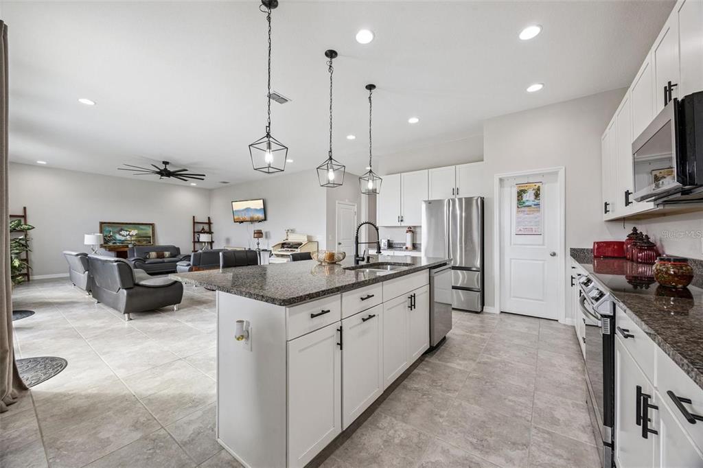 A kitchen with white cabinets, granite countertops, and an island opens into a living area — 2091 BRILLANTE DRIVE, ST CLOUD, FL