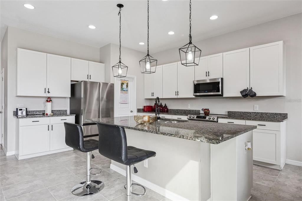 A kitchen with white cabinets, granite countertops, a center island, and three hanging pendant lights — 2091 BRILLANTE DRIVE, ST CLOUD, FL