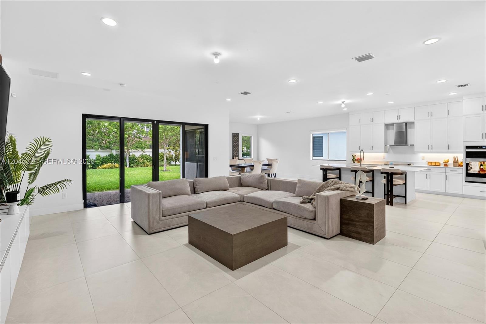 A modern open-concept living room and kitchen featuring light tile floors and sliding glass doors — 4550 SW 178th Ave, Miramar FL 33029, MIRAMAR, FL
