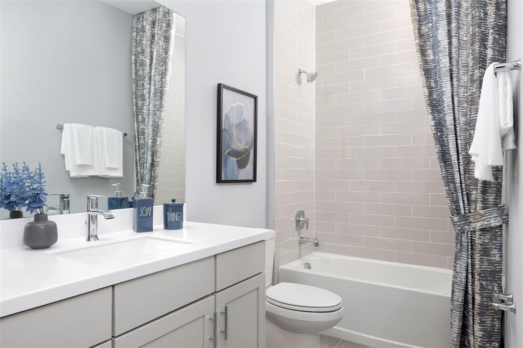 A bathroom features a gray vanity, a white countertop, a toilet, and a tiled tub-shower — 12128 MEDITATION TRAIL, VENICE, FL