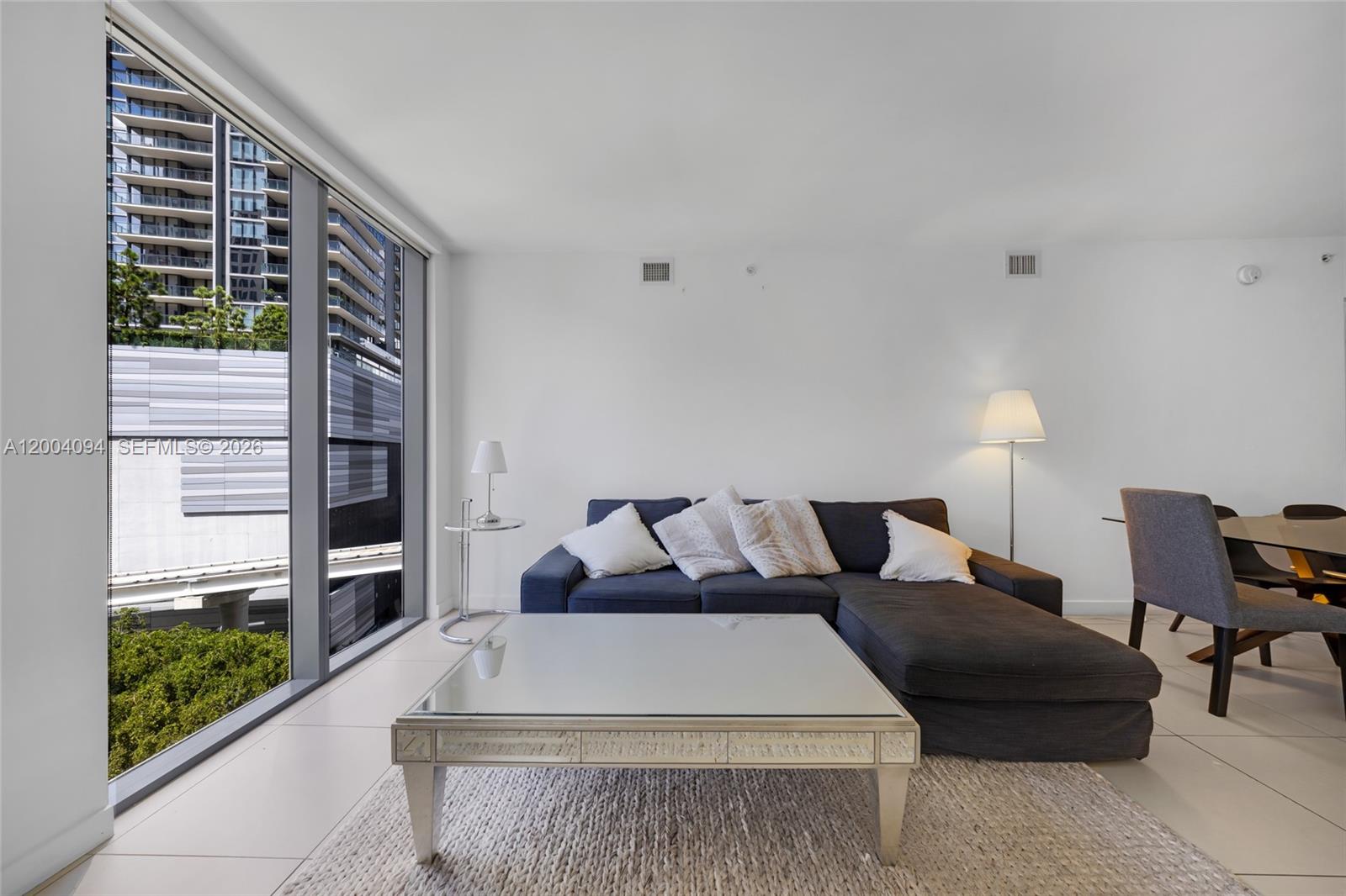A living room features a dark sectional sofa, a glass coffee table, and floor-to-ceiling windows — 31 SE 6th St # 907, Miami FL 33131, MIAMI, FL