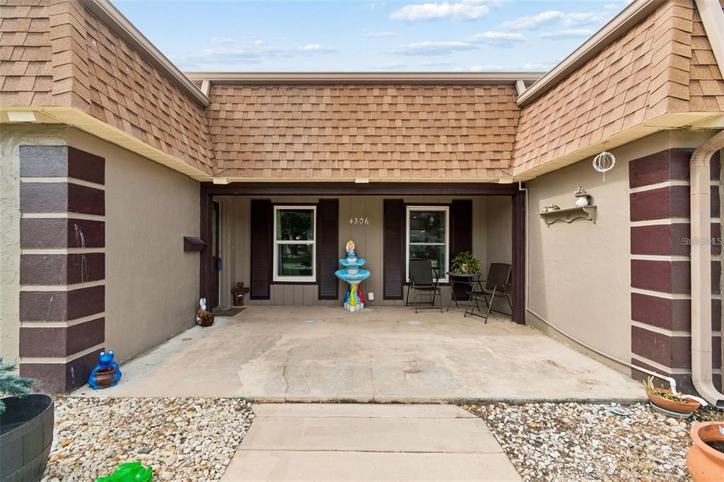 A covered concrete patio sits in front of a house with brown shutters and shingles — 4306 NEWBURY DRIVE, NEW PORT RICHEY, FL