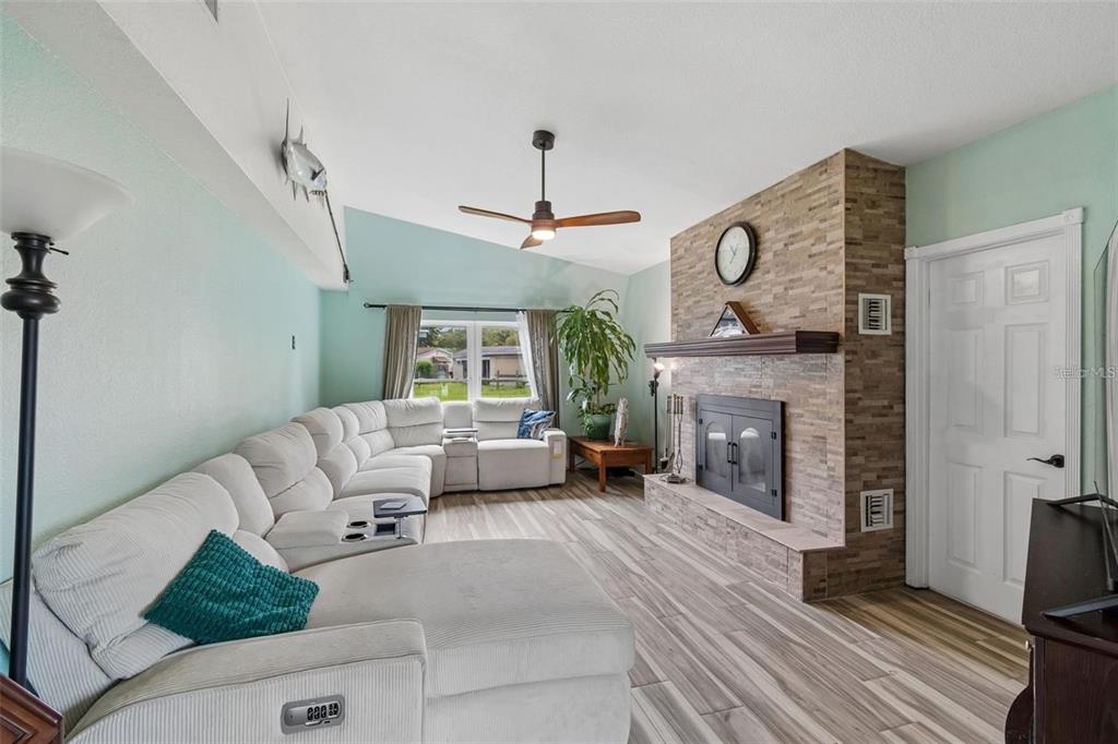 A living room features a large sectional sofa, a stone fireplace, and light wood-look flooring — 4306 NEWBURY DRIVE, NEW PORT RICHEY, FL