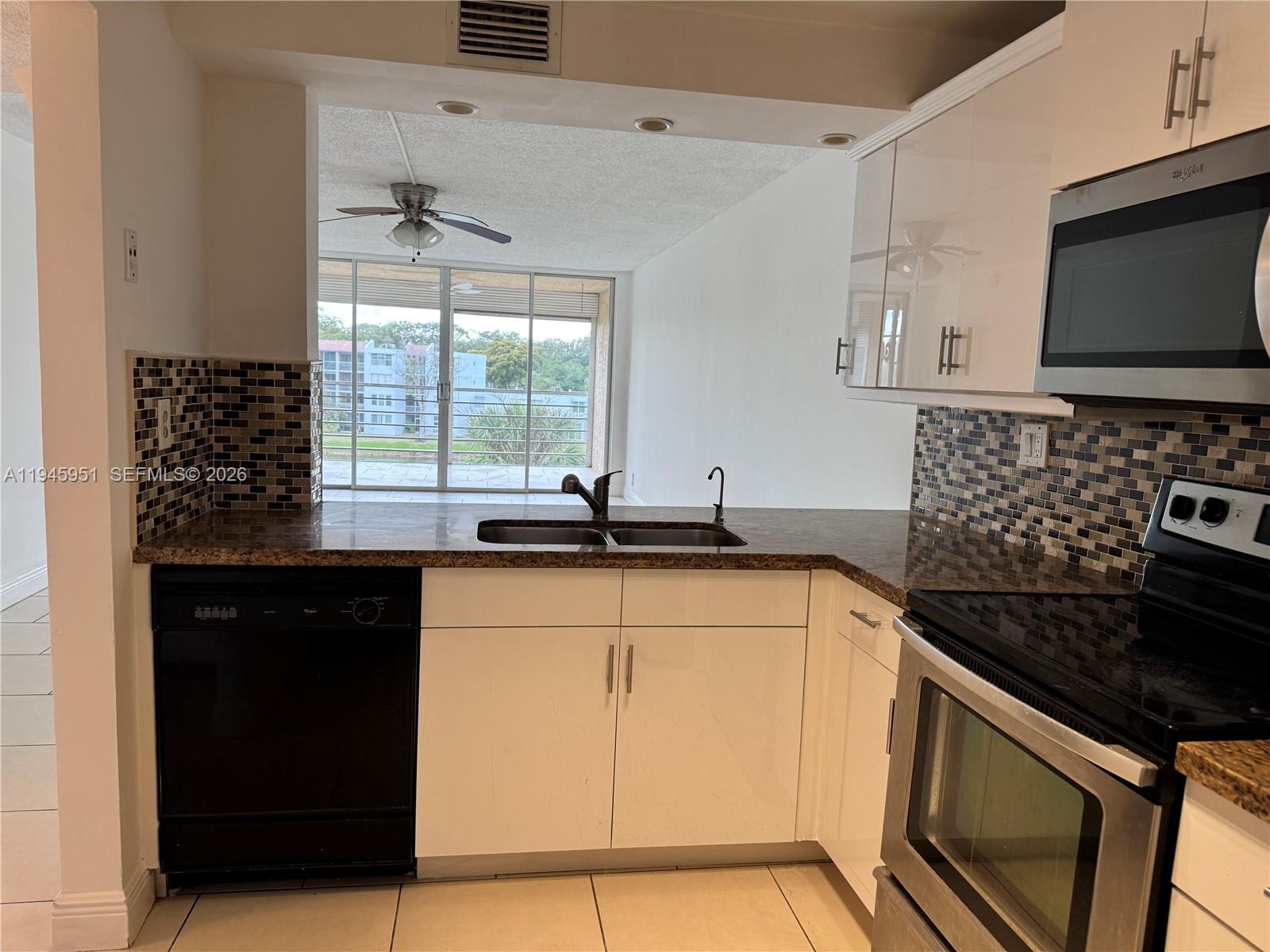 A kitchen features white cabinets, granite countertops, a mosaic backsplash, and stainless steel appliances — 1831 Sabal Palm Dr # 403, Davie FL 33324, DAVIE, FL